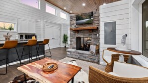 A modern kitchen with white cabinetry, a stone fireplace, and a bar area with bar stools. - Over the Moon · Sauna & Hot Tub at Modern Intimate Escape (Broken Bow)