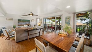 A spacious living area with a wooden dining table, a sofa, and a kitchen area with a ceiling fan. - SUMMER SALE! 3BR Condo w Sweeping Ocean Views Near the Beach - Kaanapali Plantation 32 (Lahaina)