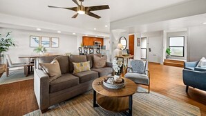 A spacious living room with a modern ceiling fan, a dining area with a wooden table and chairs, and a kitchen in the background. - SUMMER SALE! 3BR Condo w Sweeping Ocean Views Near the Beach - Kaanapali Plantation 32 (Lahaina)