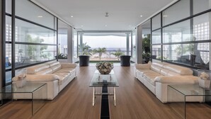 A modern living room with a glass coffee table, two white leather sofas, and a view of the beach. - Private Sunset Beach - Sea View Studio Room (Sattahip)