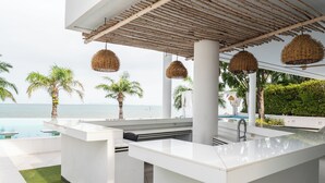 A modern outdoor kitchen with a pool, white countertops, and hanging wicker lights. - Private Sunset Beach - Sea View Studio Room (Sattahip)