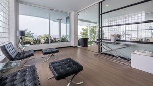 A modern interior with black leather seating, large windows, and a view of the outdoors. - Private Sunset Beach - Sea View Studio Room (Sattahip)