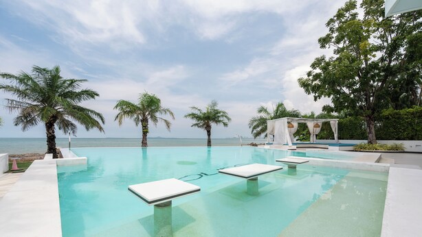 An infinity pool with clear blue water, surrounded by palm trees and a white gazebo. - Private Sunset Beach - Sea View Studio Room (Sattahip)