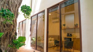 A room with a large tree, sliding glass doors, a bed, a desk, and a chair. - Hotel Florita39 (Isla Mujeres)