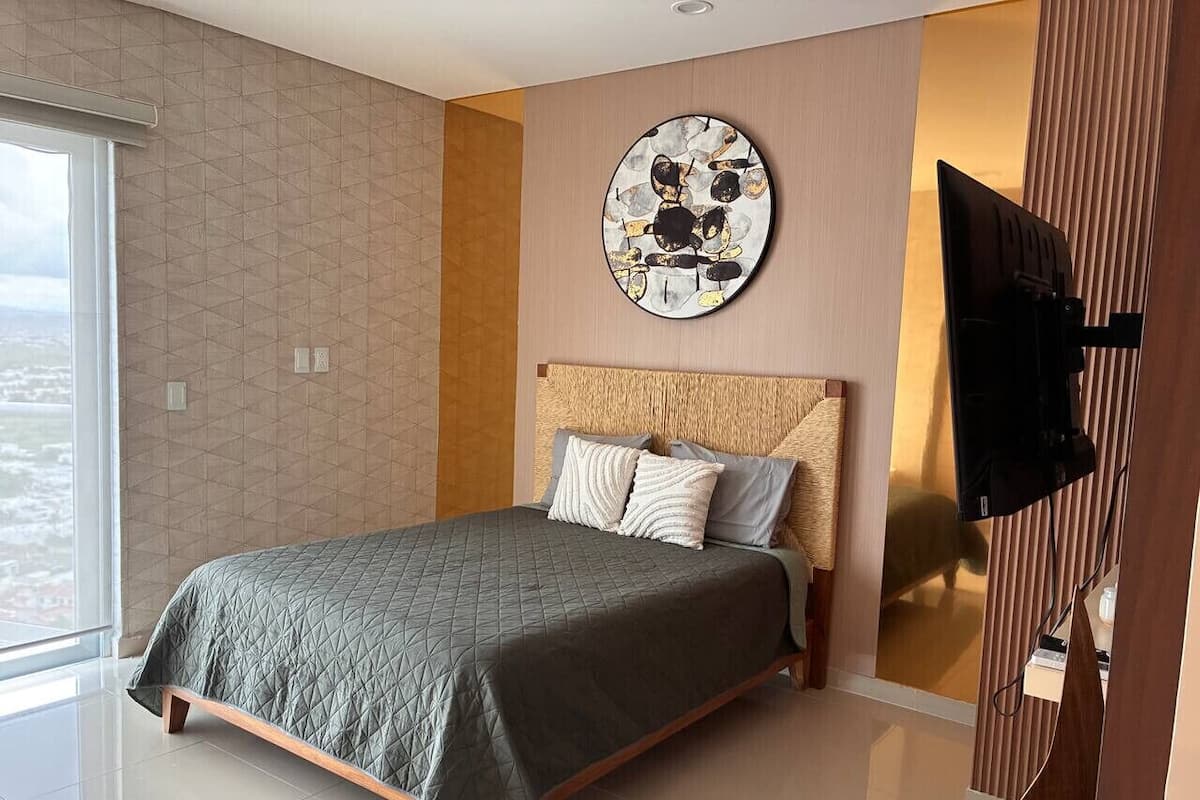 Une chambre moderne avec un lit, une grande fenêtre et un téléviseur fixé au mur.