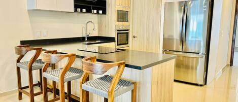 A modern kitchen with a central island, bar stools, stainless steel appliances, and wooden cabinetry.