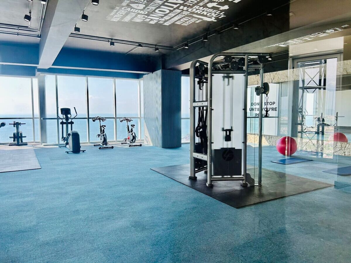 A modern gym with exercise equipment, large windows, and a motivational quote on the wall.
