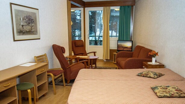 A hotel room with a bed, two armchairs, a desk, and a television. - Kylpylä-hotelli, huone 242 by Interhome (Ikaalinen)