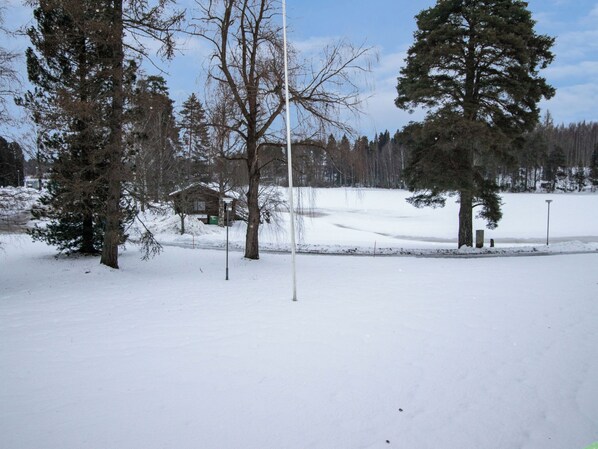 A snowy landscape with a clear sky, trees, and a building in the distance.