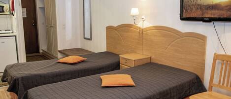 A hotel room with two beds, a television, and a wooden chair.