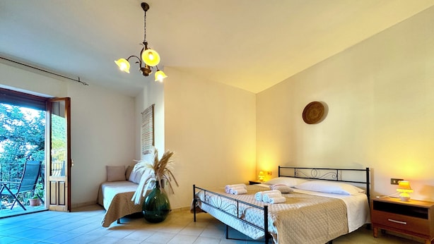 Une chambre à coucher avec un lit, des tables de chevet, une chaise, une plante en pot et une vue sur l’extérieur.