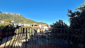 Une cour avec un portail en métal, un mur de pierre et une vue sur des maisons et une montagne en arrière-plan.