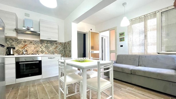 Une cuisine moderne avec des meubles blancs, une table à manger avec des chaises et un canapé gris.