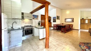 Une cuisine moderne équipée d’une cuisinière à gaz, d’un four et d’un évier, un coin repas avec des meubles en bois, et un salon avec un canapé.