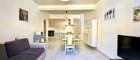 A modern living room with a sofa, a TV, and a dining area with chairs and a table.