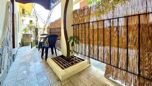 A covered outdoor area with a tiled floor, a small planter with a single tree, and a bamboo fence. - " La Corte della Pavoncella " (Bari Sardo)