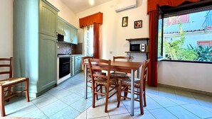 A compact kitchen with a dining area, a microwave, and a window with curtains. - " La Corte della Pavoncella " (Bari Sardo)