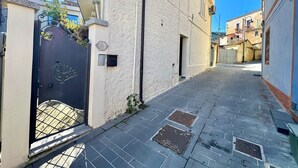 A narrow street with a gated entrance, a building with a textured facade, and a clear blue sky. - " La Corte della Pavoncella " (Bari Sardo)