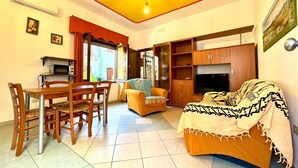 A living room with a dining area, a sofa, a TV, and a ceiling fan. - " La Corte della Pavoncella " (Bari Sardo)