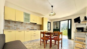 Uma cozinha compacta com armários amarelos, uma mesa de jantar com cadeiras, um sofá e uma TV sobre um suporte.