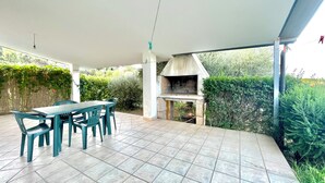 Um pátio externo com mesa e cadeiras, churrasqueira e piso de azulejos.