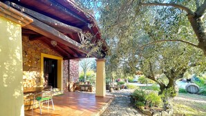 A stone building with a tiled patio, outdoor seating, and a stone pathway leading to a covered area with a pergola. - " La Pergola Deluxe " (Jerzu)