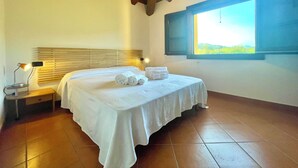 A neatly made bed with white linens and rolled towels, a bedside lamp, and a window with a view of greenery. - " La Pergola Deluxe " (Jerzu)