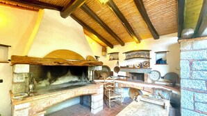 A rustic kitchen with a stone oven, wooden beams, and shelves with dishes. - " La Pergola Deluxe " (Jerzu)