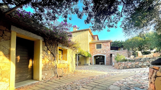 Un patio con pavimento de piedra, un edificio amarillo con una puerta cerrada y un muro de piedra.