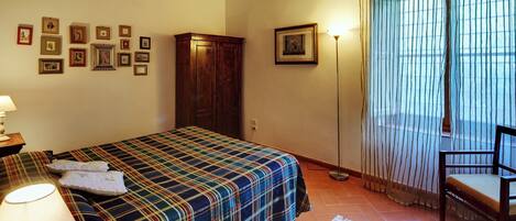 Un dormitorio con cama, armario de madera, lámpara, silla, alfombra y ventana con cortinas.