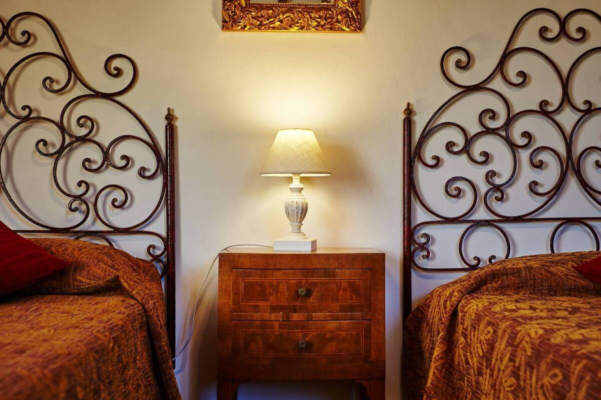 A hotel room with two beds, a nightstand with a lamp, and a decorative mirror on the wall.