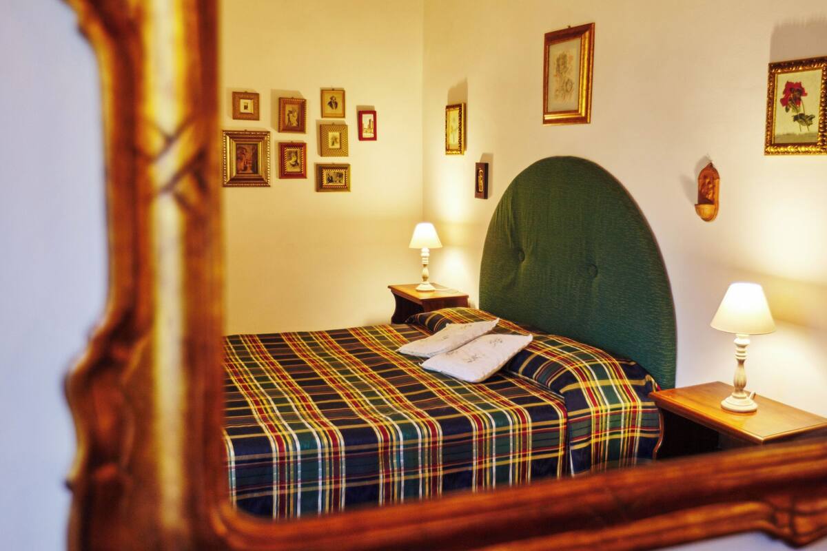 A hotel room with a plaid bedspread, a green upholstered headboard, and multiple framed pictures on the walls.