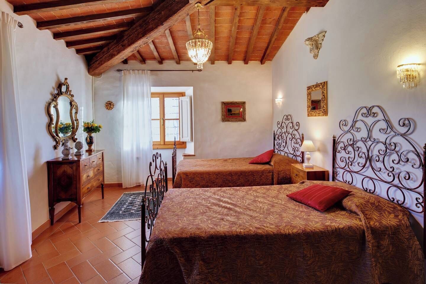 Una camera da letto con due letti, soffitto in legno, un lampadario e una finestra con tende.