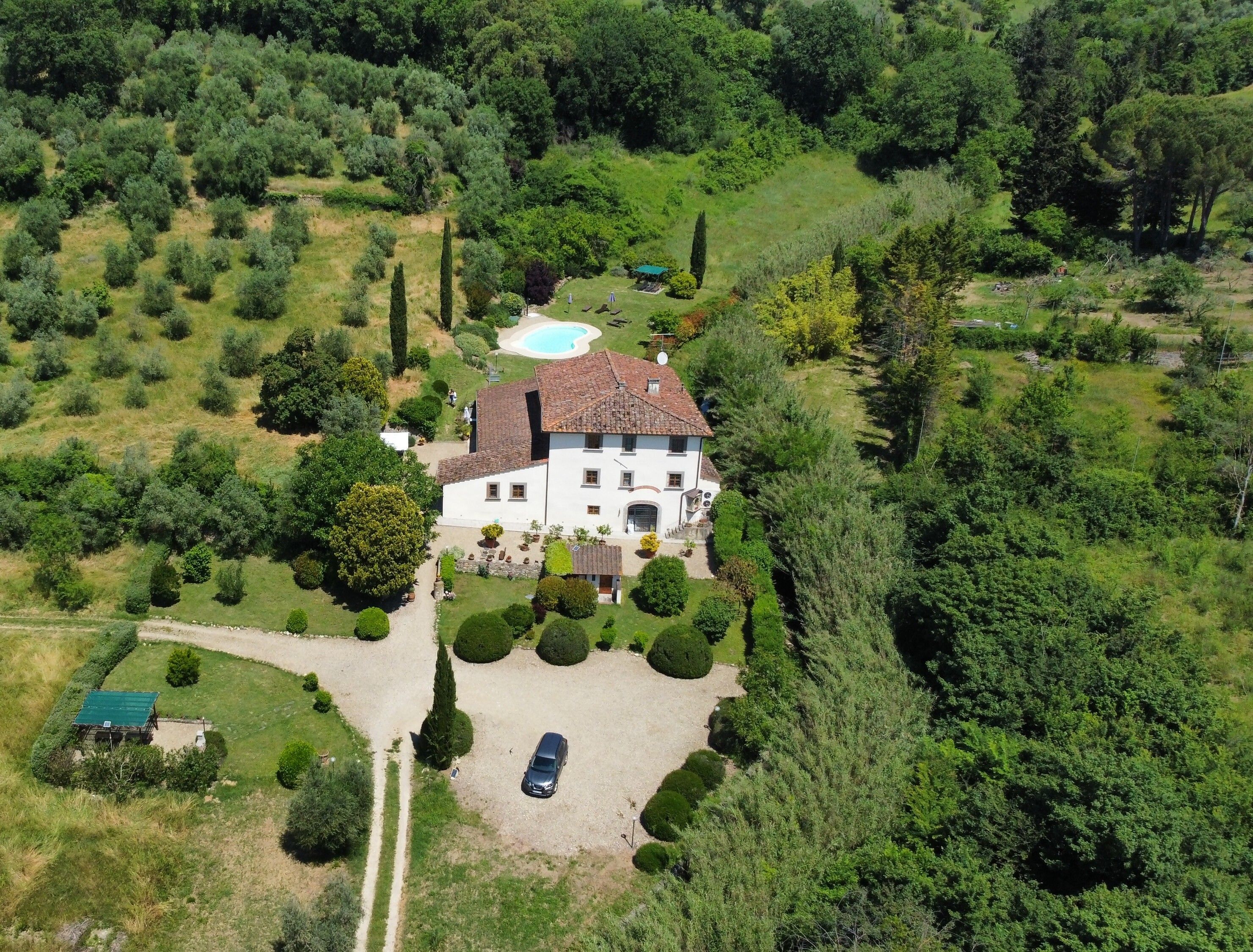 Una vista aerea di una grande casa con piscina, immersa nel verde e circondata da un prato curato.