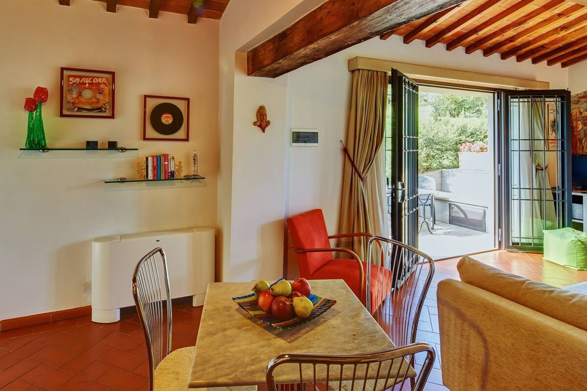 A dining area with a table set for two, a red chair, and a sofa.