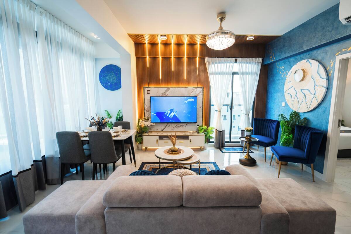 Una sala de estar moderna con un televisor grande, un sofá y un comedor con sillas y una mesa.