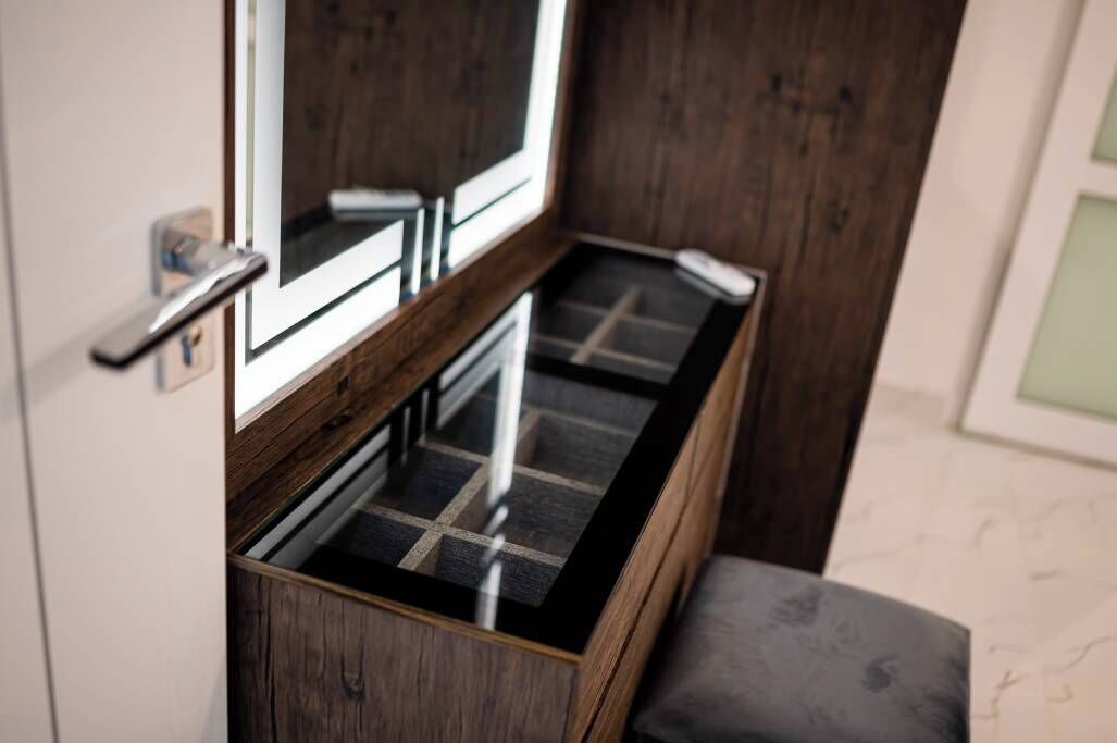 Un banc en bois avec un plateau en verre, une porte dotée d’une poignée et un miroir placé au-dessus.