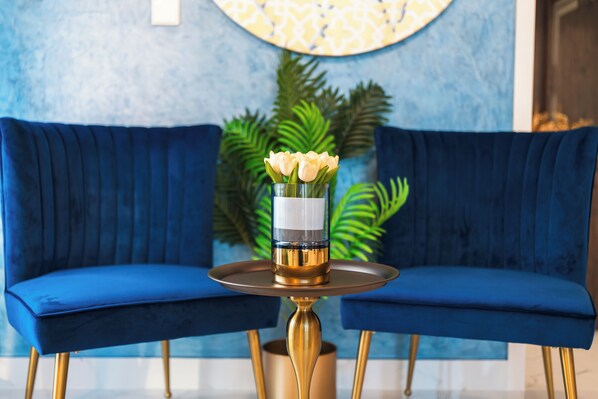 A blue sofa with a gold table in front, a vase with flowers, and a patterned wall in the background. - Aina Residency Beachfront Hotel (Hulhumale)
