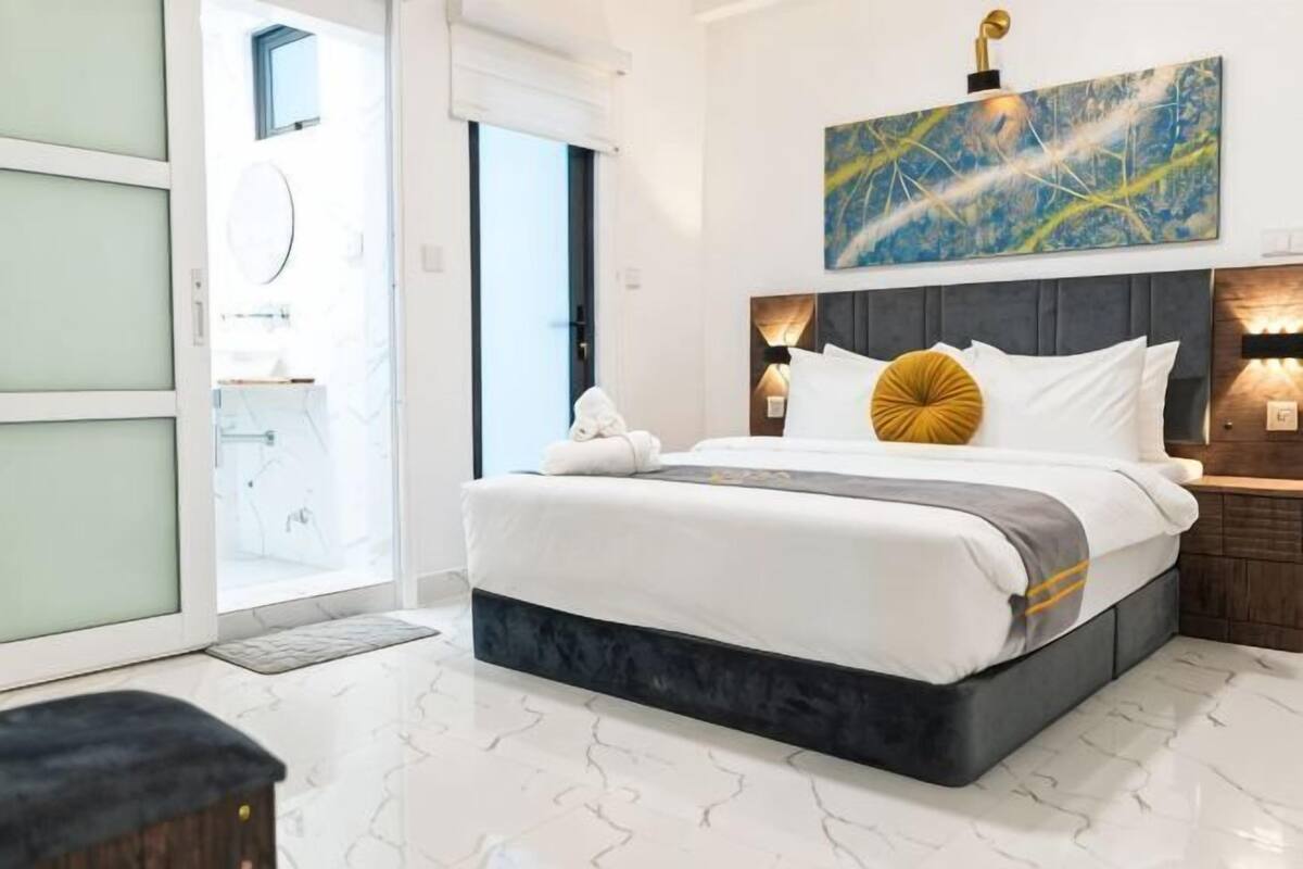 Una habitación de hotel moderna con una cama grande, un baño con un espejo redondo y una puerta que da a un área exterior.