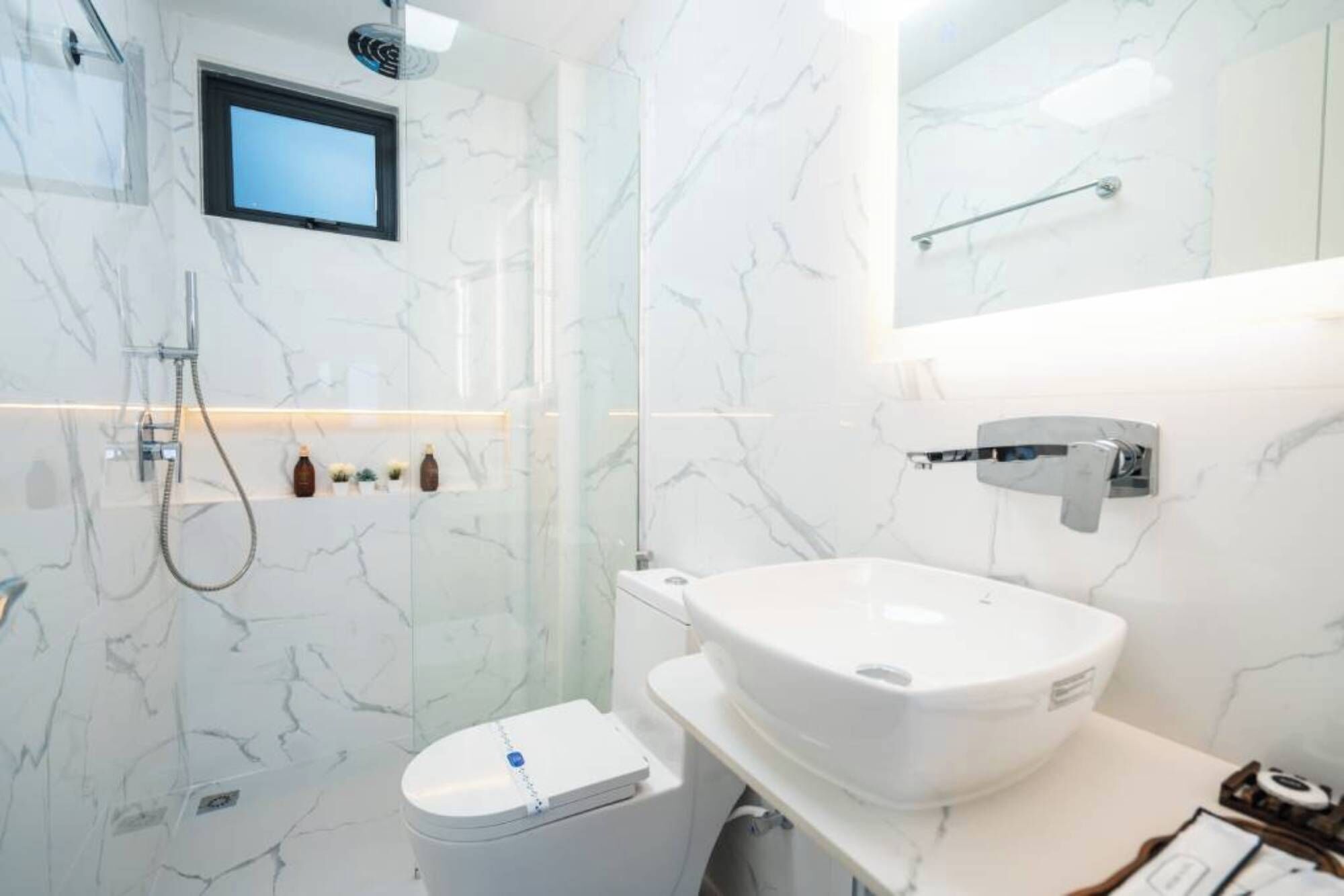 Ein modernes Badezimmer mit weißer Marmor-Spritzschutzwand, integrierter Toilette, einem weißen Waschbecken und einer Handbrause.