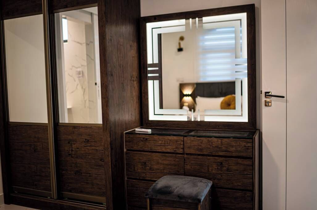 A room with a large mirror, wooden dresser, and a bench.
