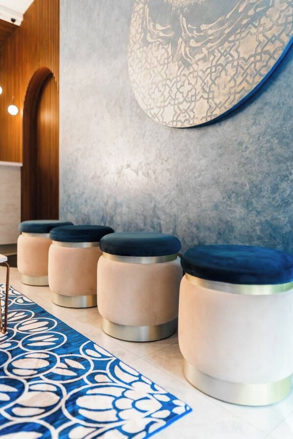 A modern interior with a row of round stools with dark tops, a patterned rug, and a textured wall with a circular design. - Aina Residency Beachfront Hotel (Hulhumale)