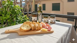 A table with bread, cheese, and cured meats on a balcony with a view of buildings.
