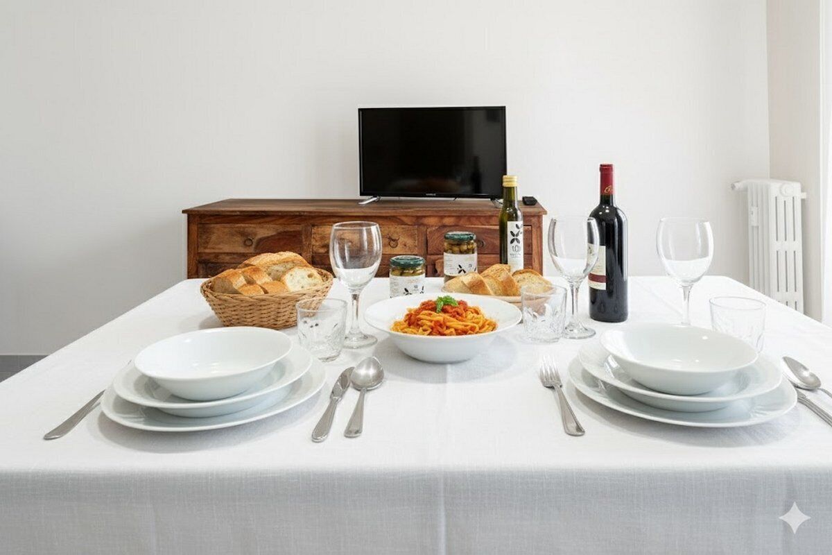 A dining table set with plates, glasses, and a bottle of wine, with a television and wooden cabinet in the background.