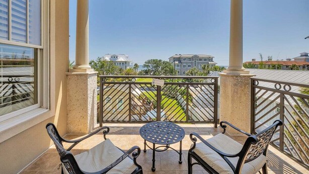 A balcony with a table and two chairs, overlooking a residential area with houses and a green lawn. - One bedroom with Oceanviews! (Saint Simons Island)