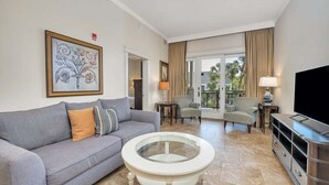 Un salon moderne avec un canapé gris, une table basse en verre, un téléviseur à écran plat et un balcon avec vue.
