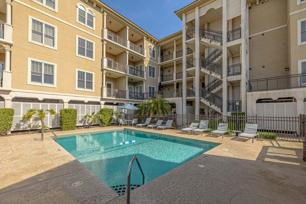 A multi-story hotel with a swimming pool, outdoor seating, and a staircase.