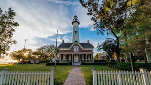 A lighthouse museum with a brick pathway leading to the entrance, surrounded by white picket fences and trees. - One bedroom with Oceanviews! (Saint Simons Island)