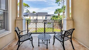 A balcony with two chairs and a table, overlooking a residential area with houses and trees. - Gorgeous condo-luxurious interiors, fantastic amenities, near fun St. Simons activities! (Saint Simons Island)