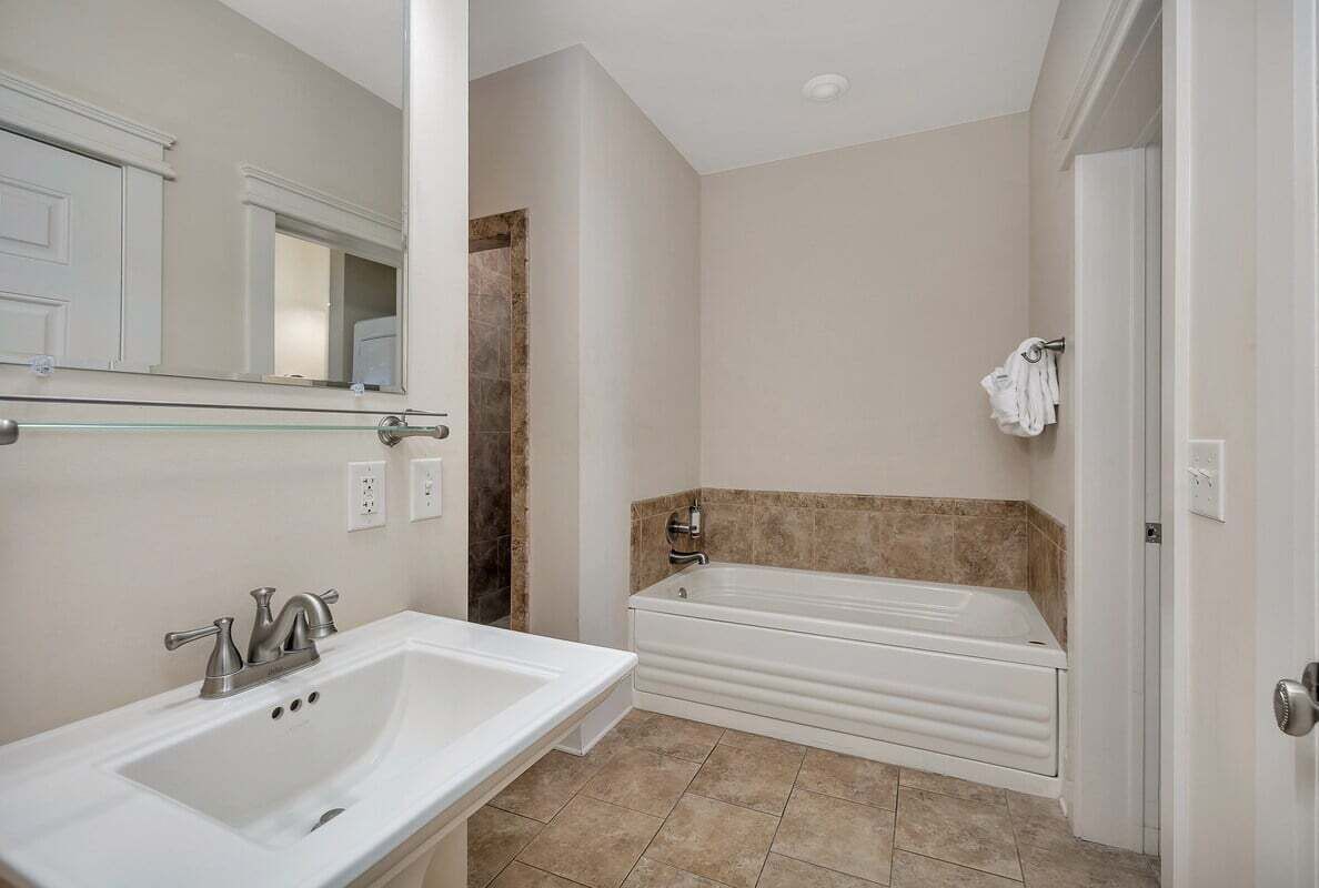A bathroom with a white sink, a bathtub, and a mirror.
